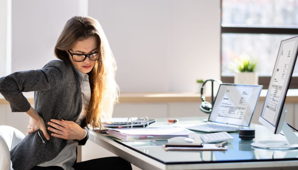 Woman holding her lower back in pain at an office desk