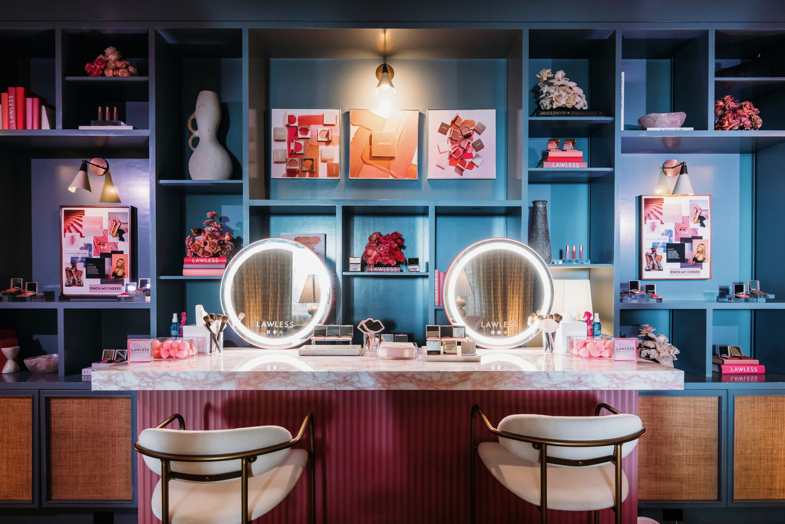 Lawless beauty brand event vanity station with two illuminated round mirrors and teal shelving wall with brand products