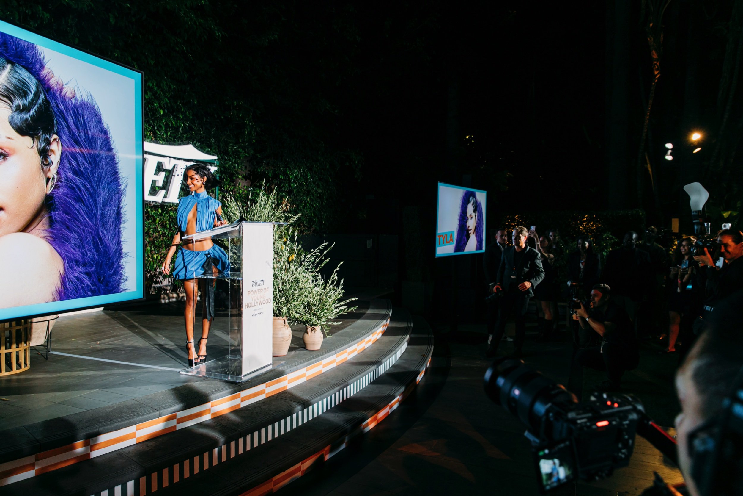 Variety Power of Young Hollywood event — presenter at a podium on stage with a large screen showing a portrait and audience in background