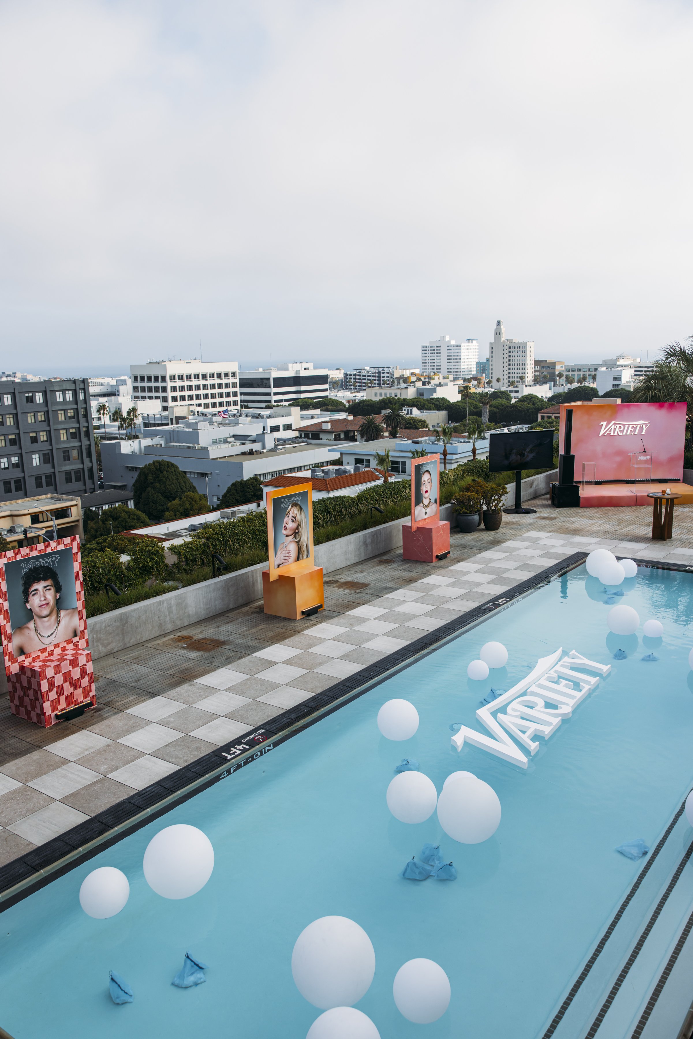 Rooftop pool event setup for Variety Power of Young Hollywood, with floating balloons, the Variety logo in the pool, celebrity portrait displays and the Los Angeles city skyline beyond