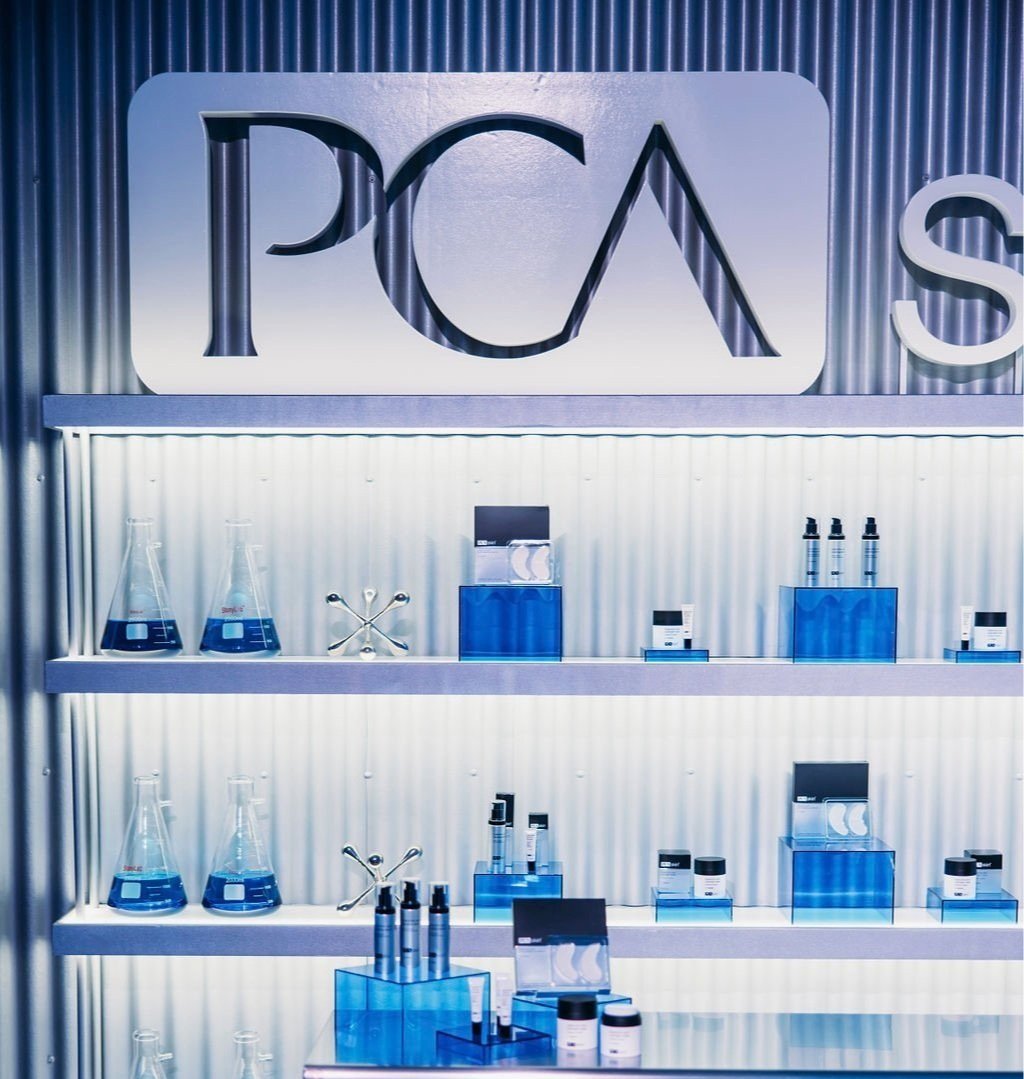 PCA Skin branded corrugated metal product display shelves with blue-lit skincare products and lab beakers
