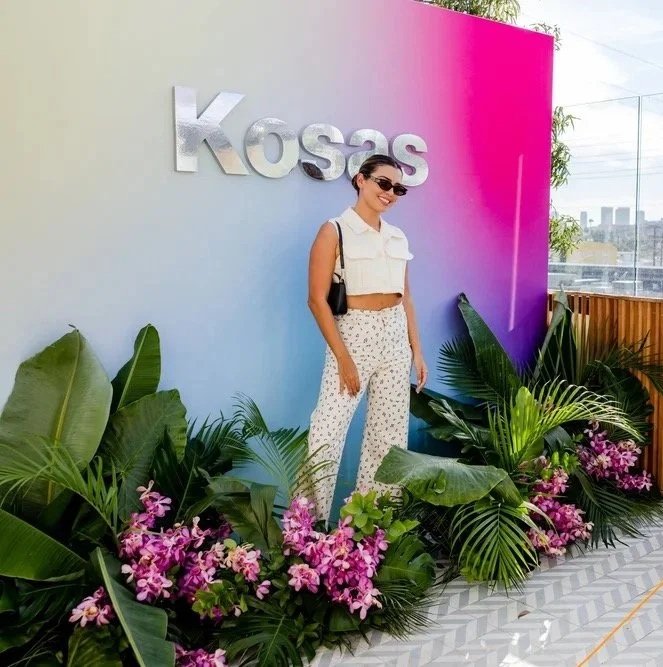 Woman posing in front of a colorful Kosas branded gradient backdrop with tropical florals