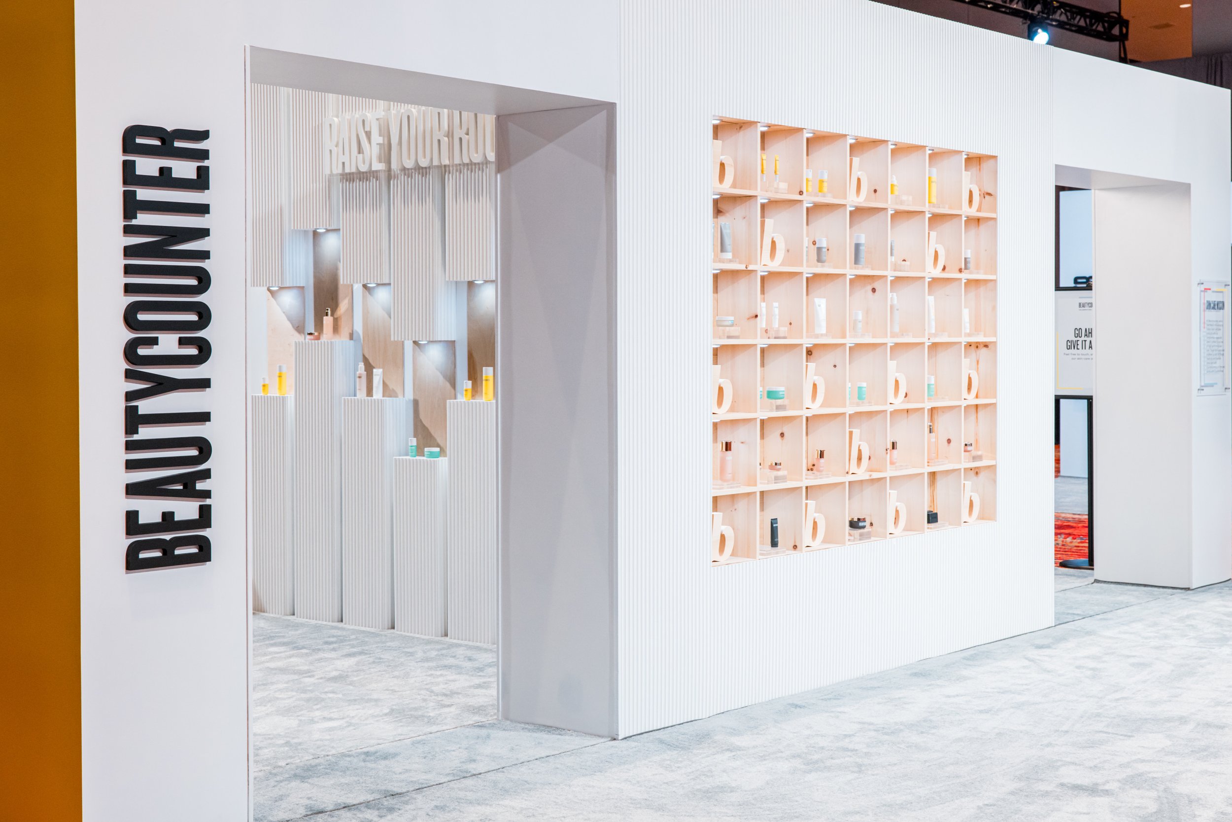 Beautycounter trade show booth exterior with bold signage, product display shelving wall and entrance archway