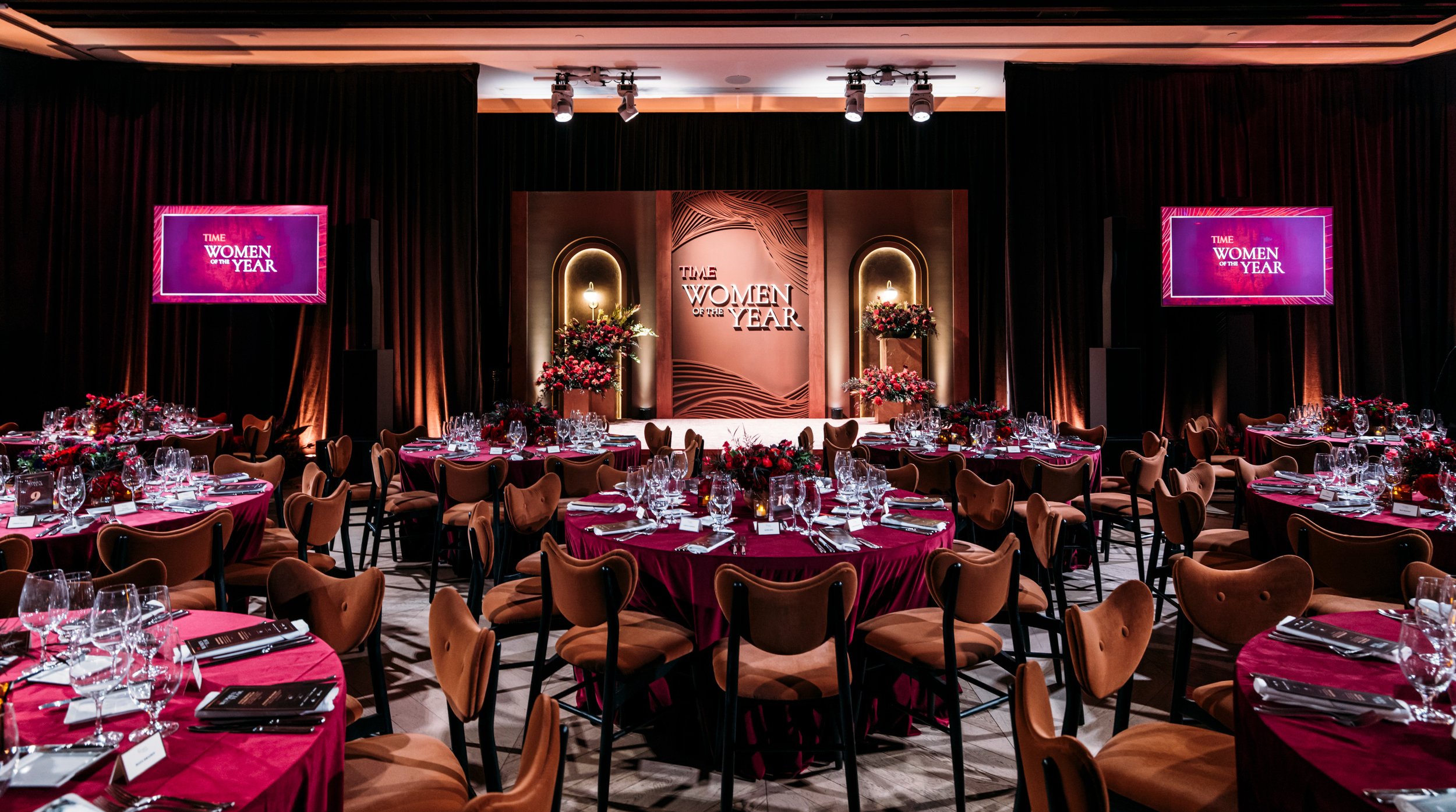 TIME Women of the Year Gala ballroom with crimson-draped round tables and ornate arched stage backdrop