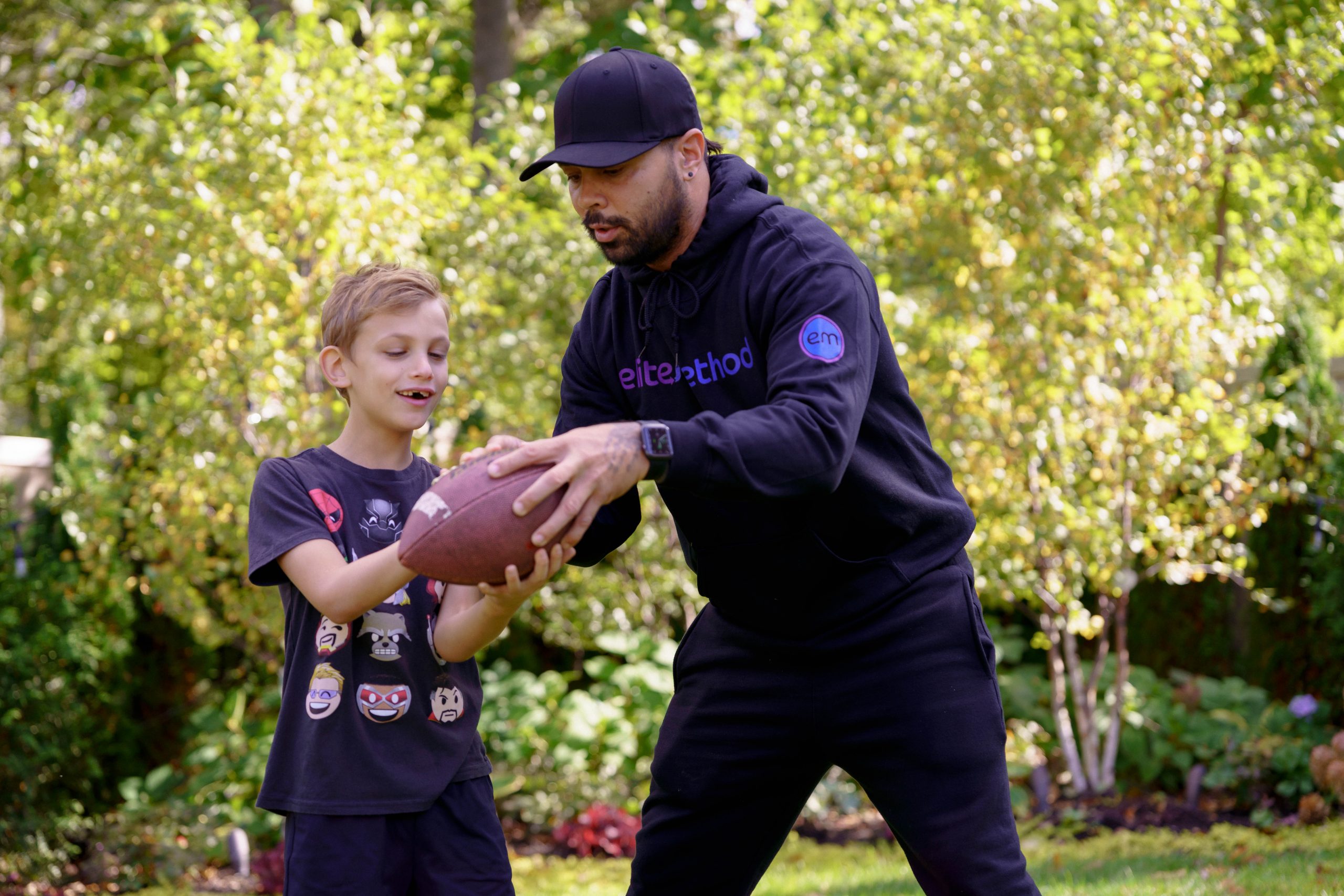 Elite Method coach teaching a young boy to hold a football outdoors