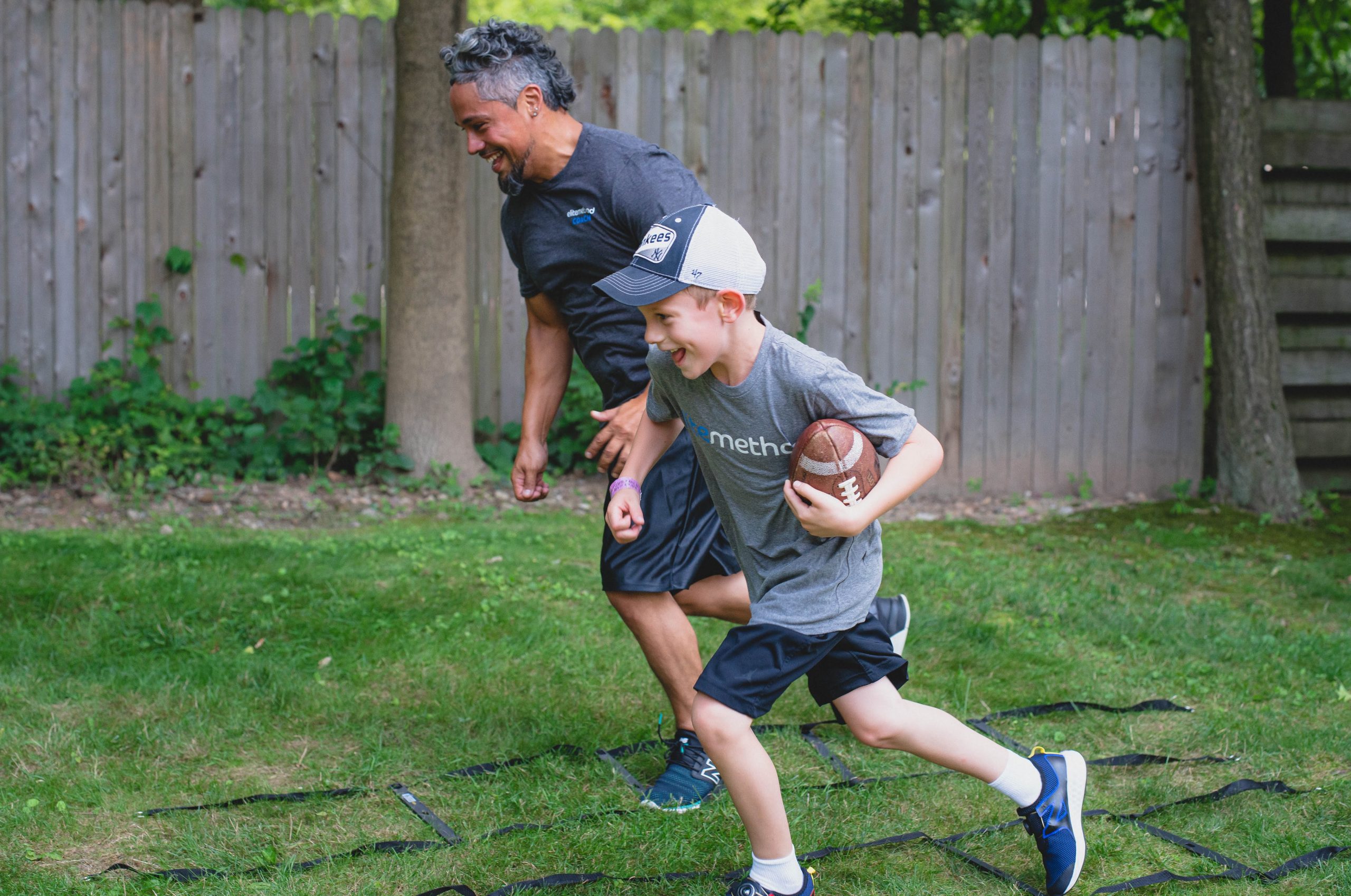 Elite Method coach chasing a smiling child running with a football through an agility ladder