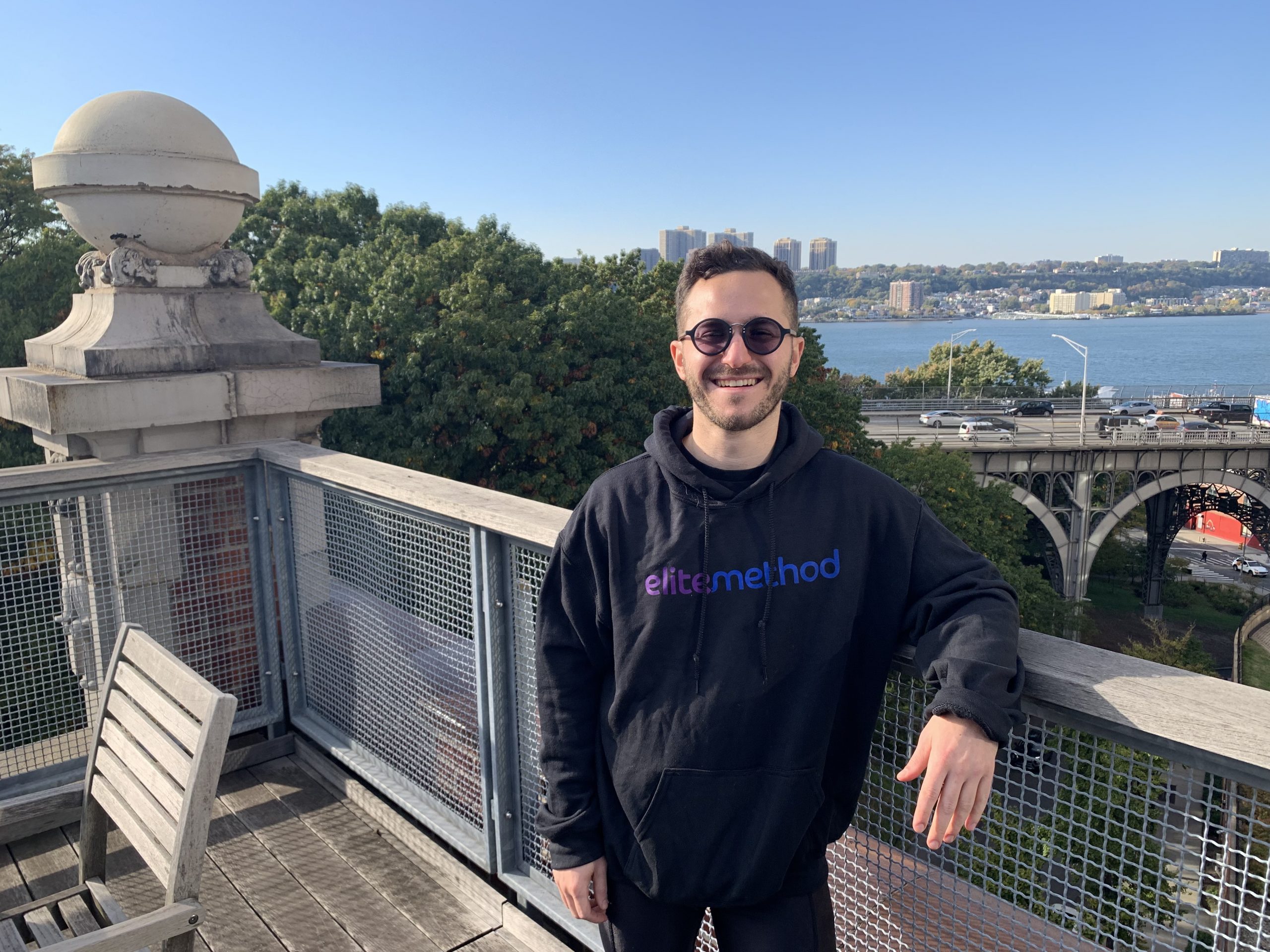 Young man in an Elite Method hoodie on an outdoor terrace with the city skyline behind him