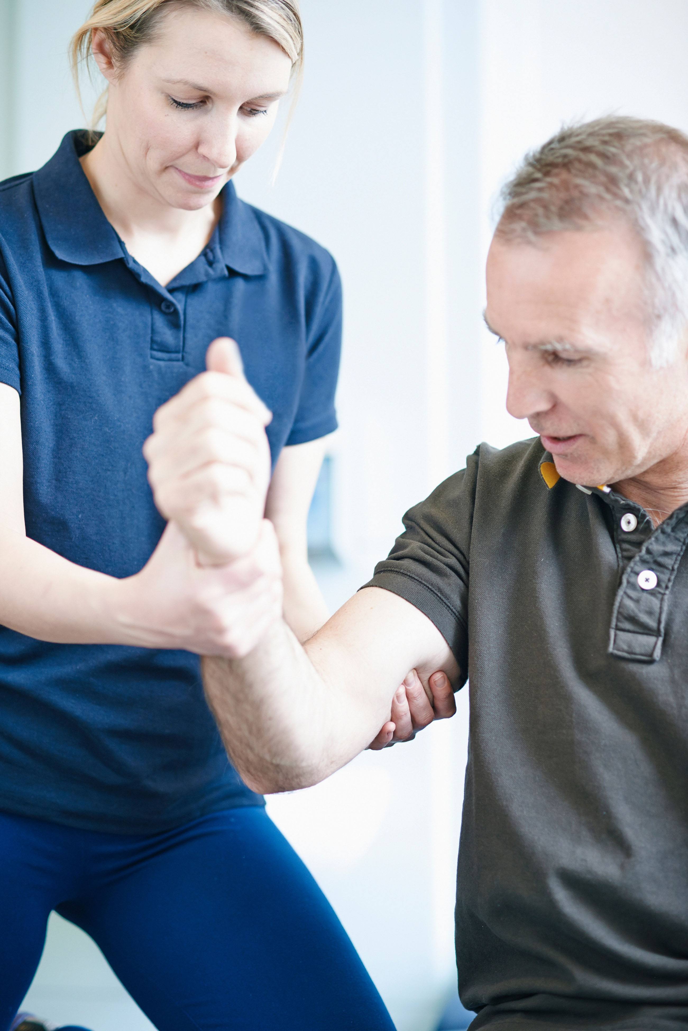 Trainer in navy polo assisting an older male client with an arm rehabilitation exercise