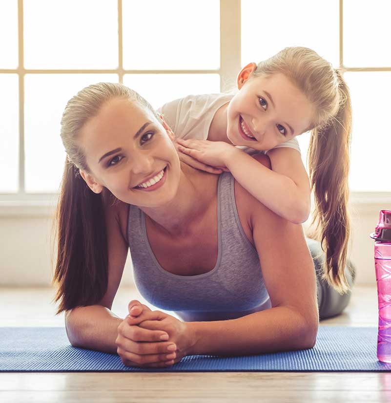 Young woman on a yoga mat with a smiling young girl on her back