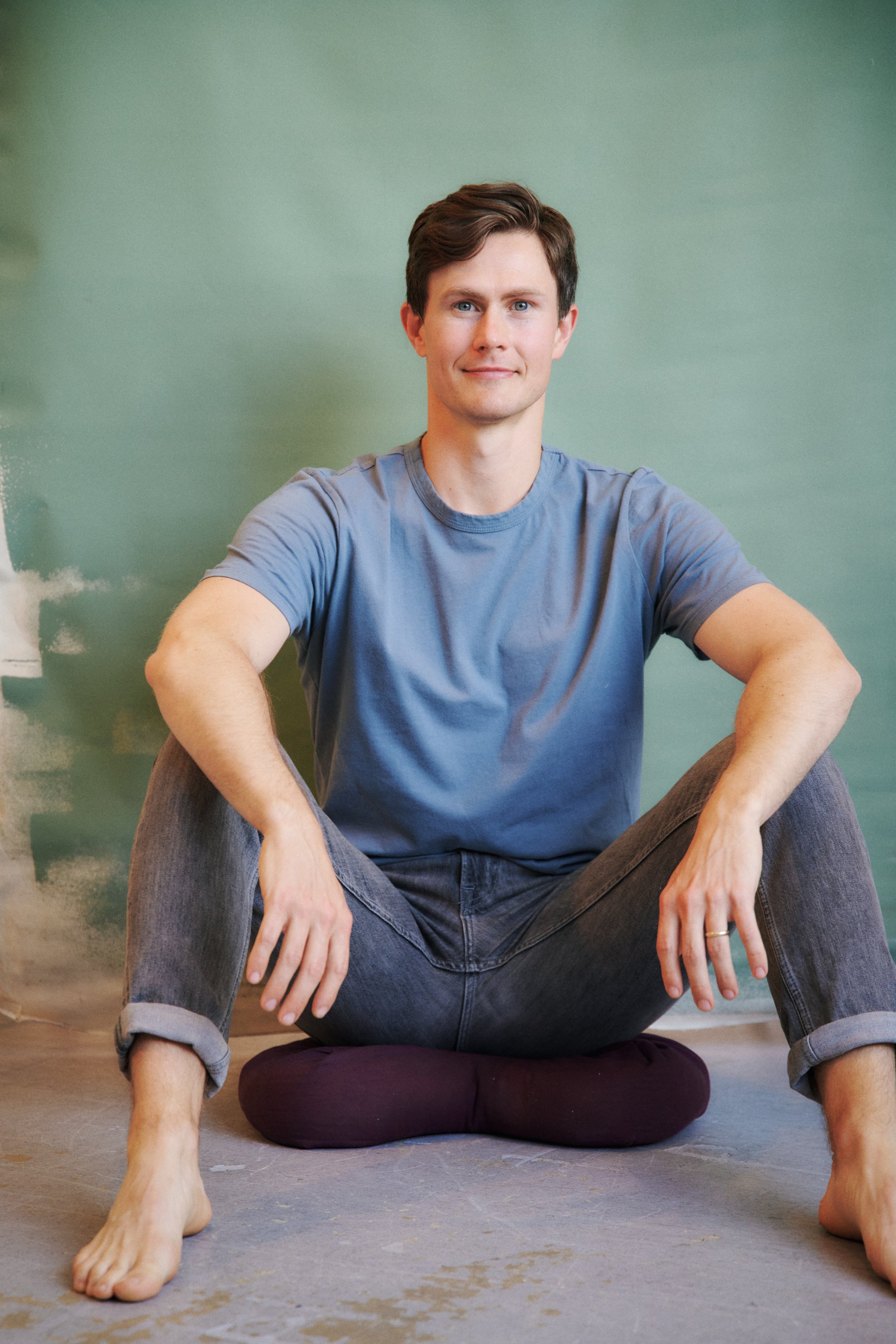 Kevin Munhall seated cross-legged against a green backdrop