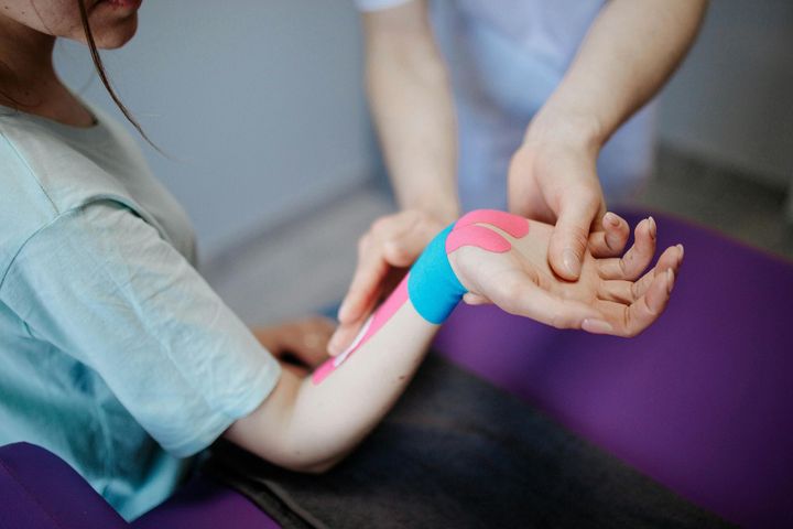 Therapist applying kinesiology tape to a patient's wrist and forearm
