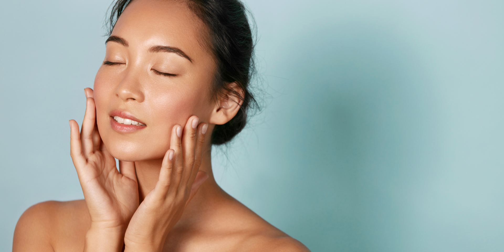 Woman with eyes closed, hands gently touching her face, calm teal background