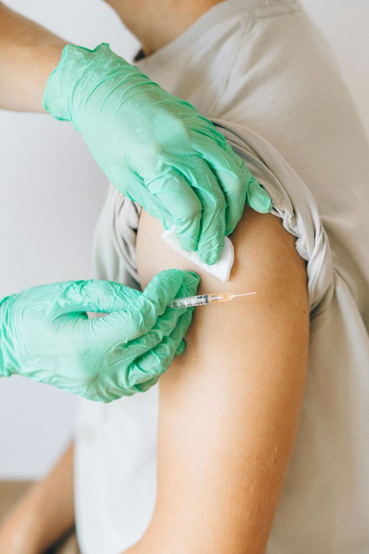Gloved hands administering an injection into a patient's upper arm