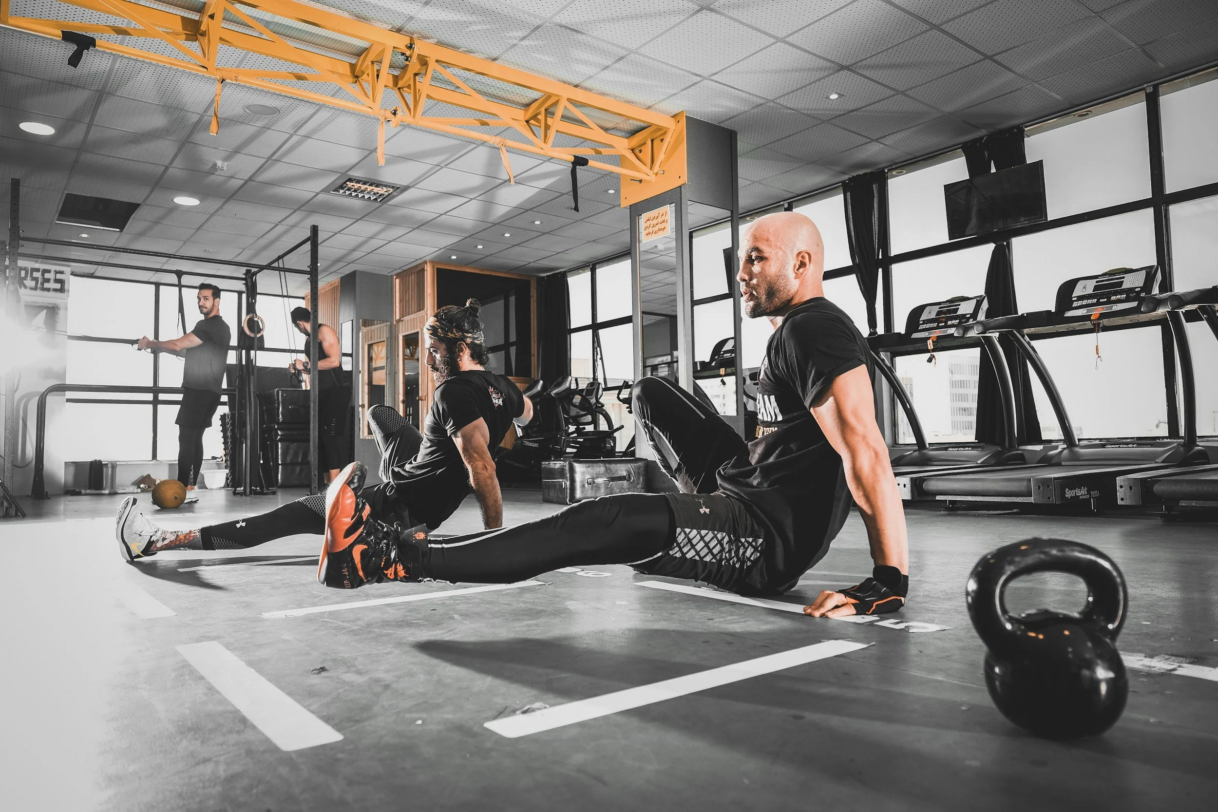 Two athletic men doing floor exercises in a desaturated gym