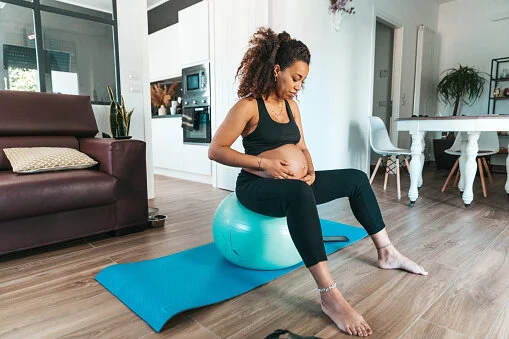 Pregnant woman sitting on an exercise ball on a yoga mat at home