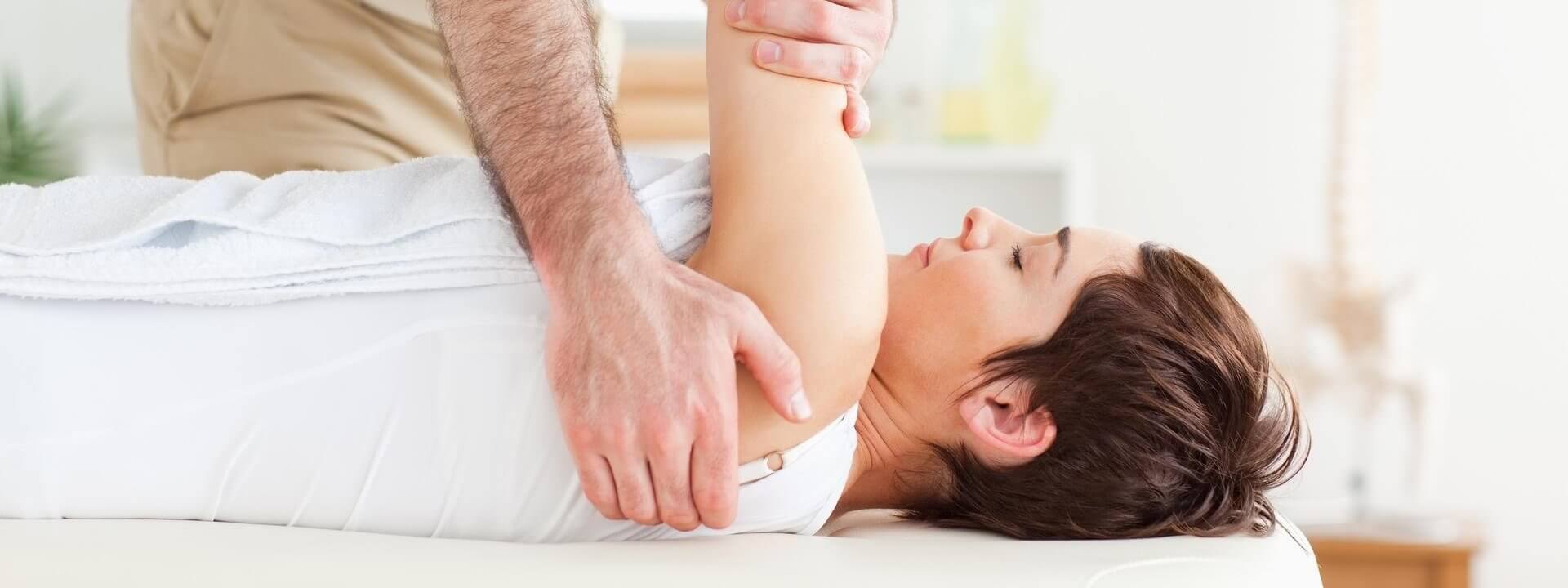 Physical therapist performing a gentle shoulder release on a patient on a treatment table